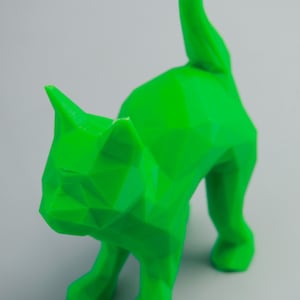 Pode incluir: Uma figurinha de gato verde de baixa poli com uma cauda longa. O gato está em pé sobre suas quatro patas com a cabeça ligeiramente inclinada para o lado.