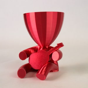 Könnte beinhalten: Eine rote 3D-gedruckte Figur eines Menschen, der Gitarre spielt. Die Figur hat einen großen Kopf und einen kleinen Körper. Die Gitarre wird in der rechten Hand der Person gehalten.