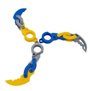 Könnte beinhalten: Drei ineinandergreifende, plastische Wurfmesser mit gelben, blauen und grauen Akzenten. Die Messer haben eine gezahnte Klinge und einen Ring am Griff.