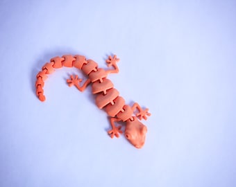 May include: A bright orange plastic toy gecko with segmented body parts and articulated limbs.