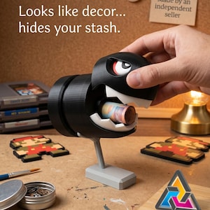 Può includere: Scatola decorativa nera e bianca a forma di Bill Ball, personaggio di Super Mario, contenente un rotolo di banconote. Il testo "Looks like decor... hides your stash" è visibile. Su una superficie di legno.