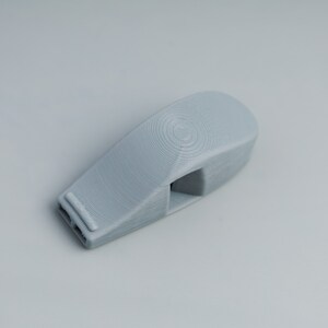 May include: A gray plastic whistle with a smooth, rounded surface. The whistle has two holes on one end and a rectangular opening on the other.