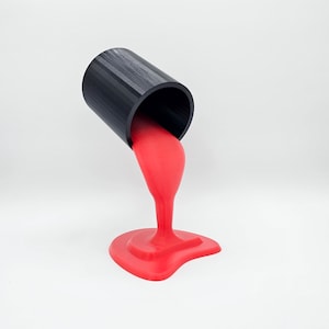 Puede incluir: Un contenedor cilíndrico negro vertiendo líquido rojo brillante en un charco sobre una superficie blanca.