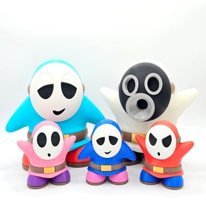 May include: Five 3D printed figures of a video game character. The figures are all different colors, including blue, pink, red, and white. The figures are all wearing masks and have different facial expressions.