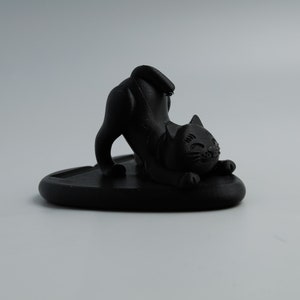 May include: Black ceramic cat figurine in a yoga pose, sitting on a heart-shaped base.