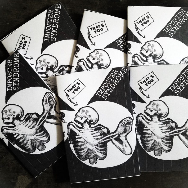 May include: A stack of black and white zines with the title "Imposter Syndrome" and a graphic of a skeleton with the text "That's You" on a white banner.