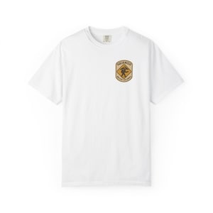 May include: White crew neck t-shirt with a small, circular patch on the chest. The patch features the text "Squamish British Columbia" around a brown and yellow graphic of a person hiking.