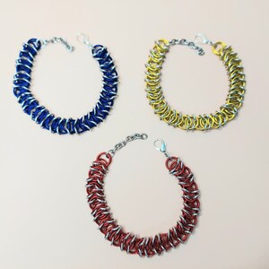 May include: Three chain bracelets in blue, yellow, and red with silver accents. The bracelets are made of metal and have a simple, elegant design.
