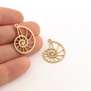 May include: Two gold-colored metal charms shaped like nautilus shells. The shells are cut out and have a detailed spiral design.