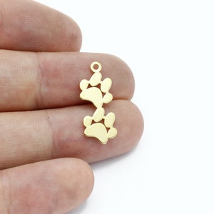 May include: Gold-toned metal charm featuring two paw prints stacked vertically. The charm has a loop at the top for attaching to a necklace or bracelet.
