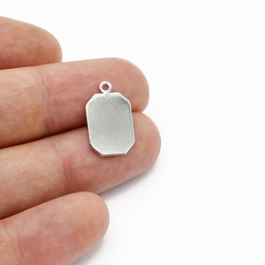 May include: Silver-toned pendant charm with a rectangular shape and a smooth, flat surface. The charm has a small loop at the top for attaching to a necklace or bracelet.