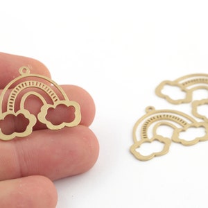 Könnte beinhalten: Goldfarbene Metall-Regenbogen-Anhänger mit Wolkenakzenten. Die Anhänger haben ein Ausschnittdesign und eine kleine Schlaufe oben zum Befestigen an Schmuck oder anderen Bastelarbeiten. Das Bild zeigt die Anhänger vor einem weißen Hintergrund.