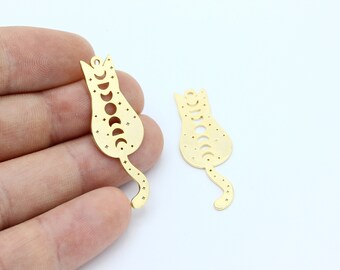 Puede incluir: Dos dijes de gato de metal dorado con un diseño de fase lunar. Los dijes están recortados en forma de gato con cola. El cuerpo del gato está lleno de pequeñas estrellas y la cola está llena de pequeñas estrellas.