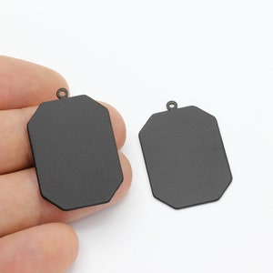 May include: Two black metal octagonal pendant charms with a loop at the top for attaching to a chain or cord.