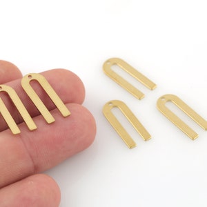 Może przedstawiać: Pięć złotych metalowych zawieszek w kształcie łuku z otworem na górze. Zawieszki mają około 2,5 cm długości.