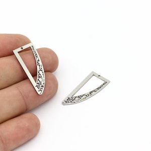 May include: Two silver-toned metal pendant charms with a decorative floral design and a rectangular cutout. The charms are shaped like a crescent moon.