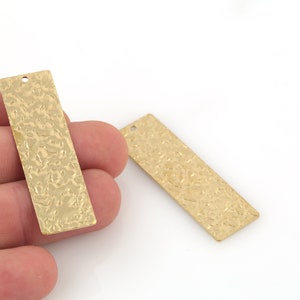 May include: Two gold-colored metal rectangular tags with a textured surface and a hole at the top.