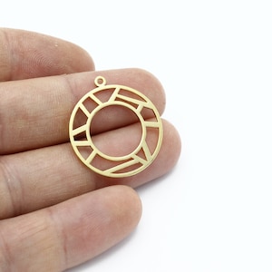 May include: A gold-colored, geometric pendant with a circular shape and an open center. The pendant features a series of straight lines and shapes that create a modern, abstract design. It has a small loop at the top for attaching to a chain or other jewelry component.