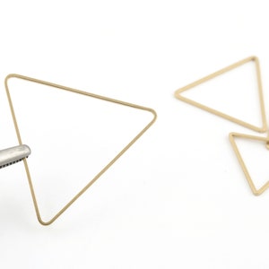 May include: A set of five gold-colored triangle-shaped metal hoops. The hoops are arranged in a pile, with one hoop being held by a pair of pliers.