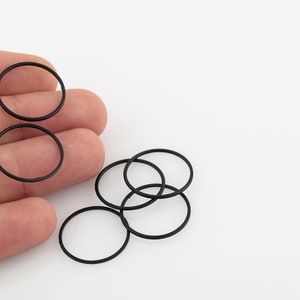 May include: A close-up of black rubber O-rings, some are stacked on top of each other, and some are held in a hand.