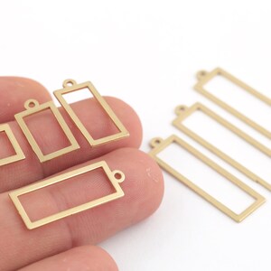 Pode incluir: Um conjunto de seis pingentes de moldura de metal dourado em v&aacute;rios tamanhos. Os pingentes s&atilde;o de forma retangular e quadrada com um pequeno la&ccedil;o na parte superior para prender a joias ou outros artesanatos.