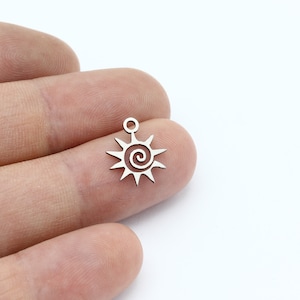 May include: Silver charm with a sun design featuring a spiral in the center. The charm has a small loop at the top for attaching to a necklace or bracelet.