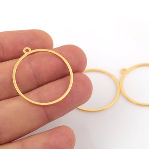 May include: Two gold-coloured metal circles with a small loop at the top. The circles are approximately 2.5 cm in diameter.
