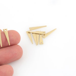Puede incluir: Un conjunto de seis abalorios de metal de forma triangular de color dorado con un agujero en la parte superior. Los abalorios miden aproximadamente 2,5 cm de largo.