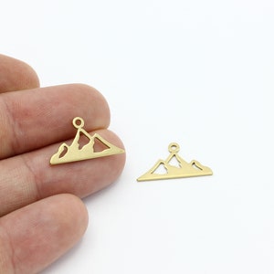 May include: Two gold-colored metal mountain charm pendants. Each pendant is shaped like a mountain range with a small loop at the top for attaching to a chain or other jewelry.