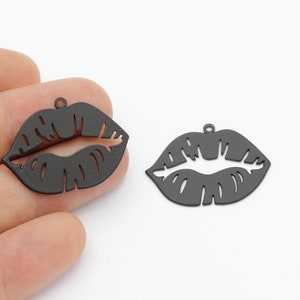 May include: Two black metal charms shaped like lips. The charms have a hole at the top for attaching to a necklace or bracelet.