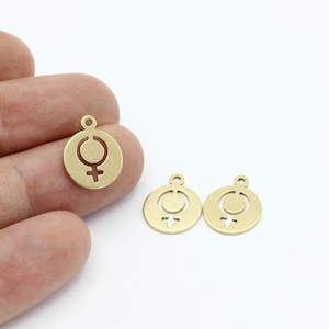 Może przedstawiać: Trzy złote metalowe zawieszki z wyciętym symbolem żeńskim. Zawieszki są okrągłe i mają małą pętelkę u góry do przymocowania do biżuterii lub innych prac rękodzielniczych.