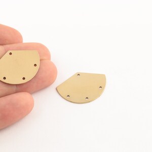 Könnte beinhalten: Zwei goldfarbene Halbkreisformen aus Metall mit jeweils fünf Löchern.