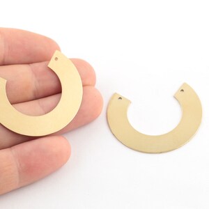 May include: Two gold-colored metal half-circle shapes with holes for hanging. The shapes are on a white surface.