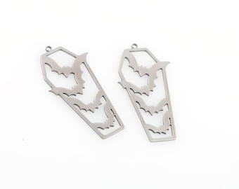 May include: Two silver metal coffin-shaped charms with cut-out bats. The charms are perfect for adding a spooky touch to jewelry or crafts.
