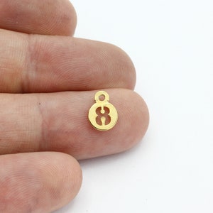 May include: Gold-colored metal charm shaped like a circle with the number 8 cut out. The charm has a small loop at the top for attaching to a necklace or bracelet.