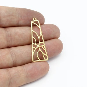Puede incluir: Pendiente de metal dorado con un diseño geométrico calado. El pendiente tiene forma de rectángulo con esquinas redondeadas y tiene un bucle en la parte superior para sujetar una cadena.