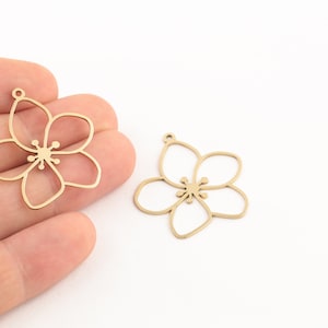 May include: Two gold metal flower charms with a delicate outline design. The charms have a loop at the top for attaching to jewelry or other crafts.