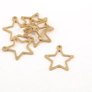 May include: A group of gold metal star-shaped charms with a hole at the top. The charms are arranged in a pile, with one charm separated from the rest.