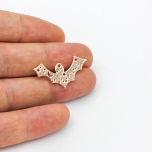 May include: Gold-colored metal bat charm with a cutout design of stars and a crescent moon. The charm has a hole at the top for hanging.