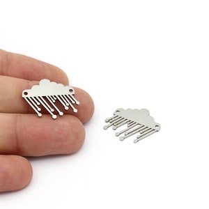 Puede incluir: Dos abalorios de metal plateado en forma de nube con gotas de lluvia que cuelgan de ella. Los abalorios tienen agujeros en la parte superior para sujetarlos a joyas u otras manualidades.