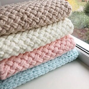 Puede incluir: Una pila de cuatro mantas afelpadas en varios colores pastel: beige, blanco, rosa y azul claro. Las mantas tienen una textura gruesa y tejida, lo que sugiere una sensaci&oacute;n suave y acogedora. Est&aacute;n cuidadosamente dobladas y apiladas.