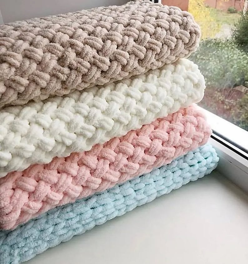 Puede incluir: Una pila de cuatro mantas afelpadas en varios colores pastel: beige, blanco, rosa y azul claro. Las mantas tienen una textura gruesa y tejida, lo que sugiere una sensaci&oacute;n suave y acogedora. Est&aacute;n cuidadosamente dobladas y apiladas.