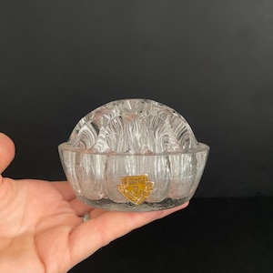 Può includere: Un vaso per fiori in vetro trasparente con un bordo smerlato e un adesivo dorato che recita "VERRERIE DE BOHEME" con un logo a corona.