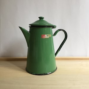 以下が含まれることがあります： 黒いハンドルと縁が付いた、ヴィンテージの緑色のエナメルコーヒーポット。ポットには蓋と注ぎ口が付いています。小さなステッカーが側面に表示されます。ポットは明るい木製の表面にあります。