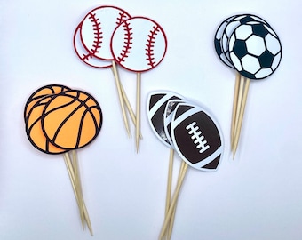May include: Set of six cupcake toppers featuring different sports balls: baseball, basketball, football, and soccer. The toppers are made of paper and have a white background with black outlines. The sticks are wooden and are approximately 3 inches long.
