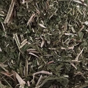 May include: A close-up of a pile of dried green herbs in a blue ceramic bowl. The herbs are finely chopped and appear to be a blend of different types.