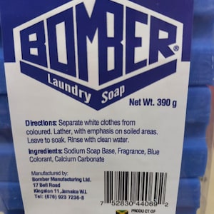 May include: A blue bar of laundry soap with the brand name "BOMBER" printed in white. The soap is packaged in a clear plastic wrapper and has a net weight of 390 grams. The product is manufactured in Jamaica.