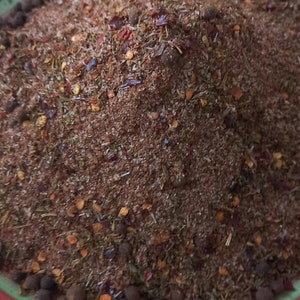 Puede incluir: Primer plano de un bol lleno de una mezcla de especias marrones, rojas y negras. Las especias incluyen hierbas secas, granos de pimienta y hojuelas de pimiento rojo.