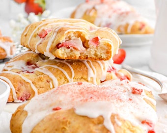 May include: Three strawberry scones with white icing and a sprinkle of red sugar. The scones are stacked on a white plate.