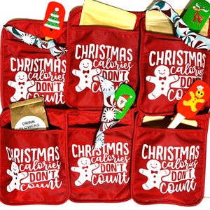 May include: Set of six red oven mitts with pockets. Each mitt features a gingerbread man graphic and the text "Christmas calories don't count". The mitts are decorated with festive ribbons and include various kitchen tools.